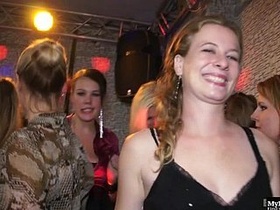 At a large gathering, a woman's skirt is pushed aside as she engages in oral sex with her partner, including a teasing lick